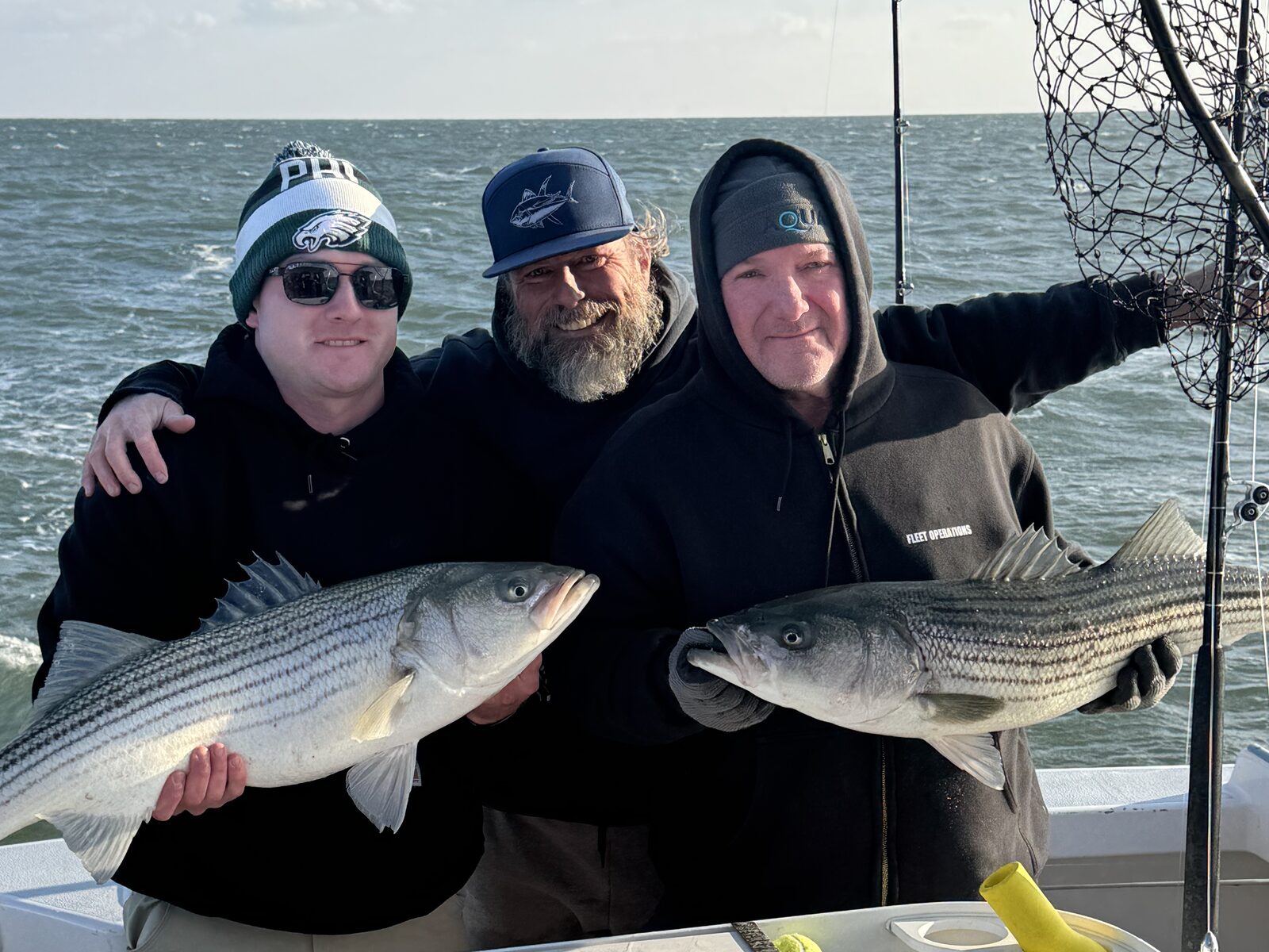 Three anglers holding striped bass aboard a boat during the LBI Cup